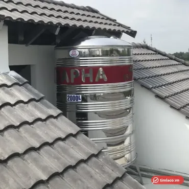 Bồn nước inox Dapha 2000 lít đứng lắp giữa hai mái ngói, băng đỏ chữ DAPHA và nhãn 2000L