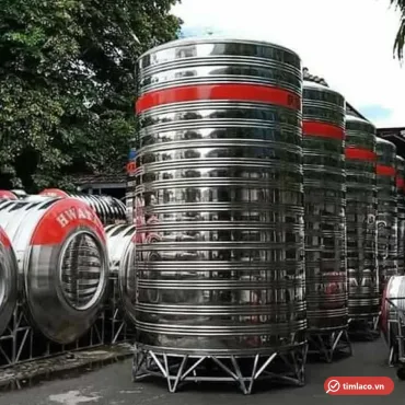 Bồn nước inox Hwata đứng cỡ lớn băng sơn đỏ trên chân inox tại bãi hàng, bên cạnh bồn ngang chữ HWATA (ảnh minh hoạ dòng hàng)