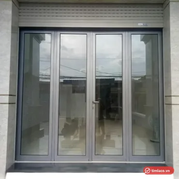 Cửa đi nhôm kính 4 cánh khung xám lắp ở mặt tiền nhà, phía trên có hộp cửa cuốn (ảnh minh hoạ)
