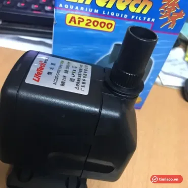 Máy bơm chìm Lifetech AP2000 thân đen có tem thông số, đầu nối ống trên cổng xả, phía sau là hộp AP2000